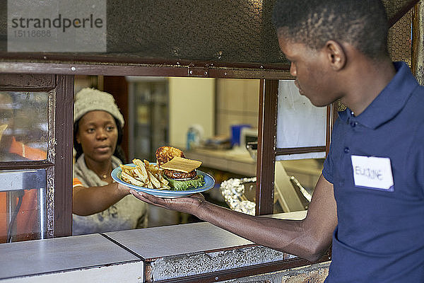 Junger Kellner  der das gelieferte Essen aus der Restaurantküche entgegennimmt  Südafrika