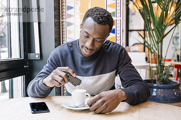 Junger Mann mit schnurlosen Kopfhörern und Handy beim Kaffeetrinken in einem Café