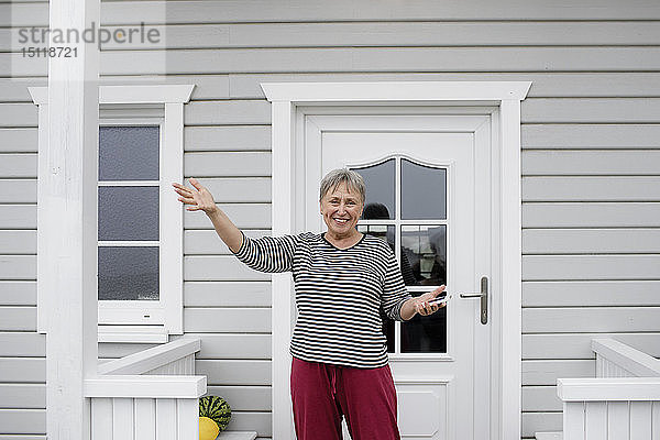 Glückliche ältere Frau steht auf der Veranda ihres Hauses