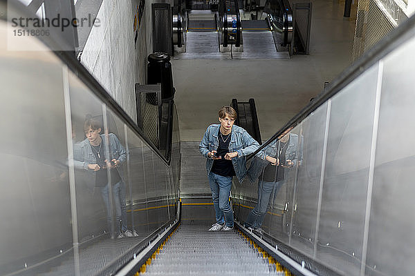 Junger Mann mit Handy auf der Rolltreppe