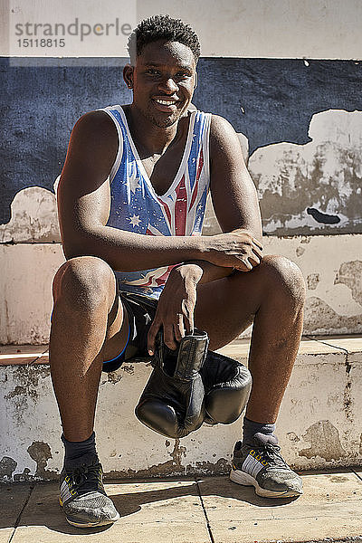 Porträt eines lächelnden Boxers mit seinen Boxhandschuhen  der nach dem Training im Freien sitzt
