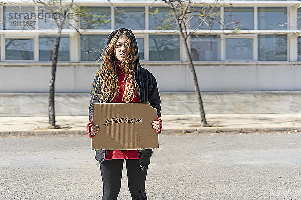 Porträt einer ernsthaften Teenagerin  die den Hashtag gegen Sexismus auf Pappe zeigt
