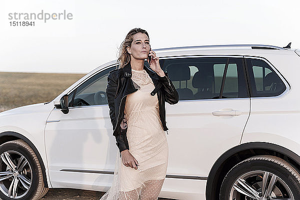 Blonde Frau mit Smartphone  weißes Auto im Hintergrund