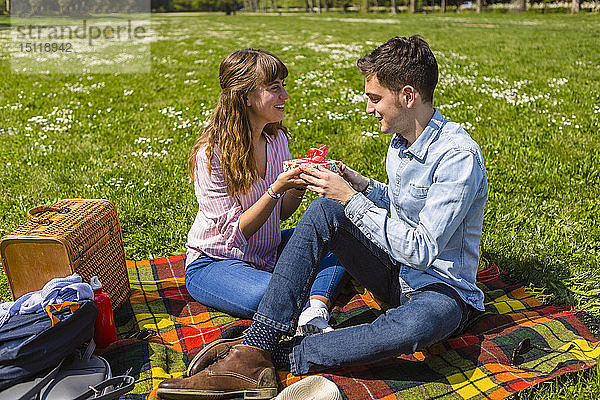 Junge Frau überreicht ihrem Freund in einem Park ein Geschenk