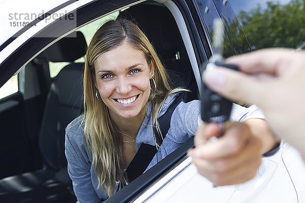 Porträt einer lächelnden jungen Frau  die in die Kamera schaut  während sie die Autoschlüssel in der Hand hält und sie jemandem durch das Fenster gibt