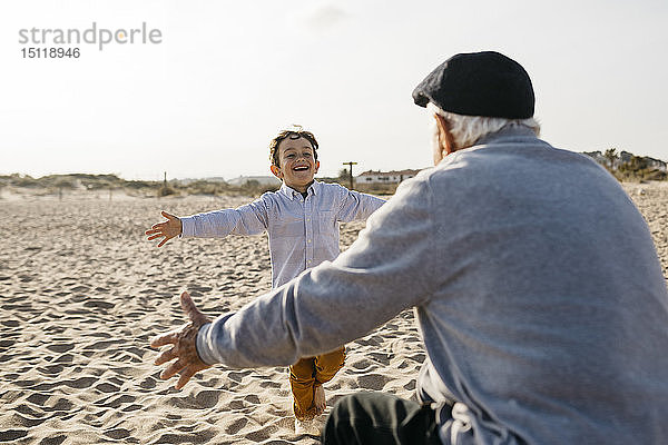Porträt eines glücklichen kleinen Jungen  der am Strand in die Arme seines Großvaters läuft