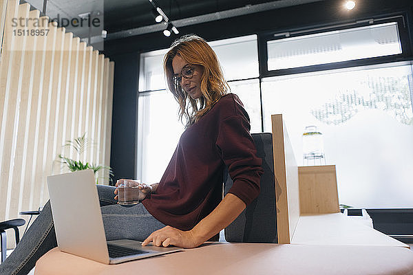 Geschäftsfrau  die im Büro am Schreibtisch sitzt und einen Laptop benutzt