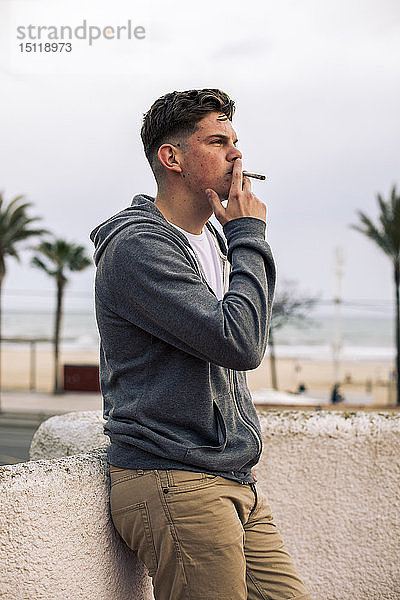 Junger Mann raucht einen Joint mit Palmen im Hintergrund