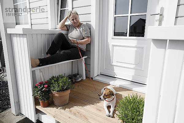 Entspannte ältere Frau sitzt mit ihrem Hund auf der Veranda