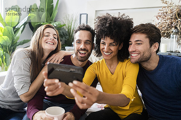 Vier glückliche Freunde sitzen auf der Couch und machen ein Selfie