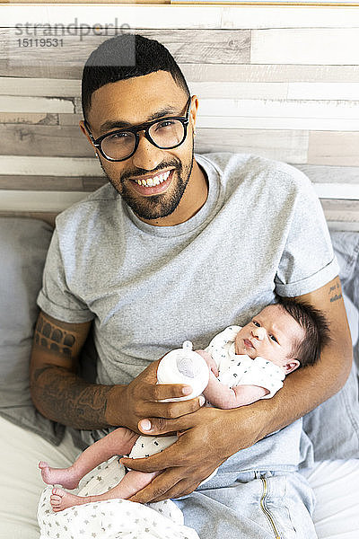 Porträt eines glücklichen Vaters  der sein Neugeborenes im Bett hält