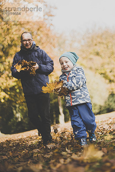 Glücklicher Vater und Kleinkind spielen mit Herbstblättern