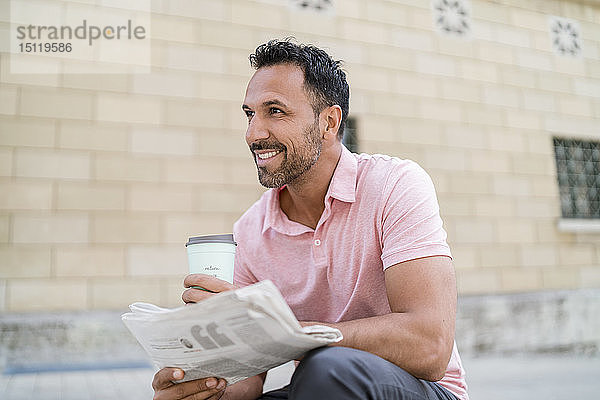 Lächelnder Mann mit Kaffee und Zeitung zum Mitnehmen in der Stadt