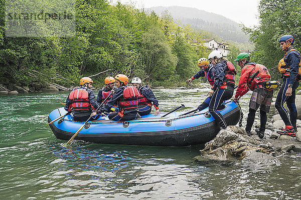 Gruppe von Personen  die mit einem Schlauchboot auf einem Fluss eine Rafting-Tour beginnen