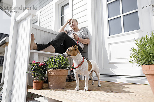 Entspannte ältere Frau sitzt mit ihrem Hund auf der Veranda