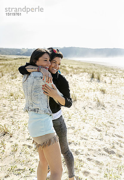 Zwei glückliche Freundinnen umarmen sich am Strand