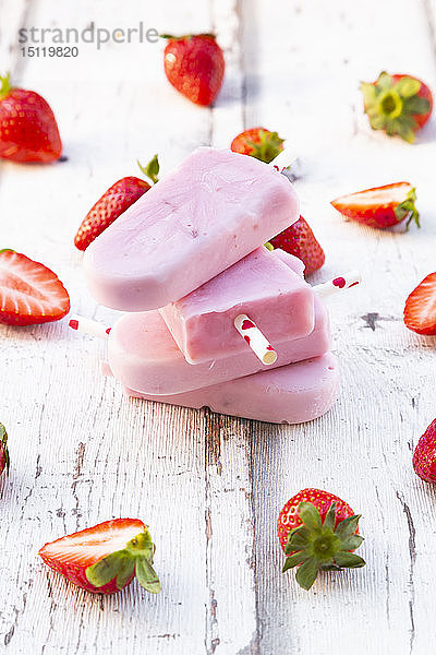 Gestapelte hausgemachte Erdbeer-Joghurt-Eislollys mit frischen Erdbeeren auf weißem Holz