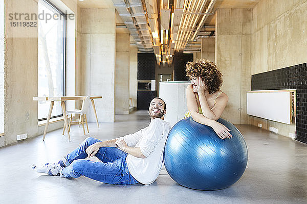 Lächelnder Mann und Frau mit Fitnessball im modernen Büro