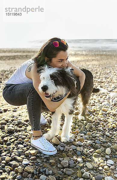 Junge Frau kuschelt mit Hund am Strand