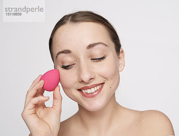 Porträt einer lächelnden jungen Frau mit rosa Schminkschwamm