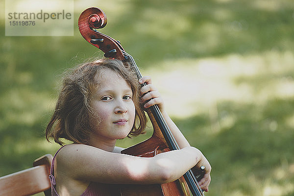 Ein Mädchen spielt Cello im Garten und schaut in die Kamera