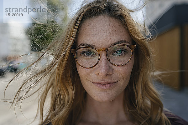 Porträt einer selbstbewussten jungen Frau mit Brille und windgepeitschtem Haar