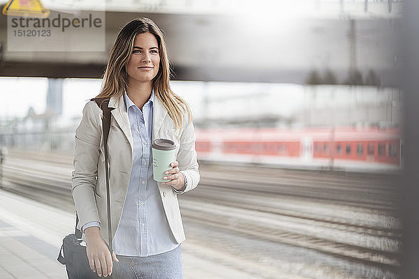 Junge Geschäftsfrau mit Kaffee zum Mitnehmen  auf dem Bahnhof stehend