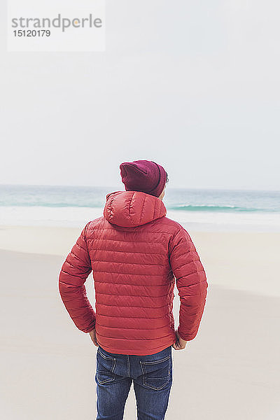 Portugal  Algarve  Sagres  Praia do Beliche  Rückansicht eines Mannes mit roter Mütze und Jacke am Strand