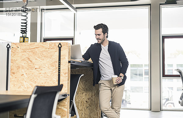 Junger Geschäftsmann im modernen Büro  mit Laptop auf dem Stehpult