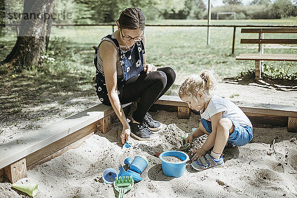 Mutter spielt mit kleiner Tochter im Sandkasten auf einem Spielplatz