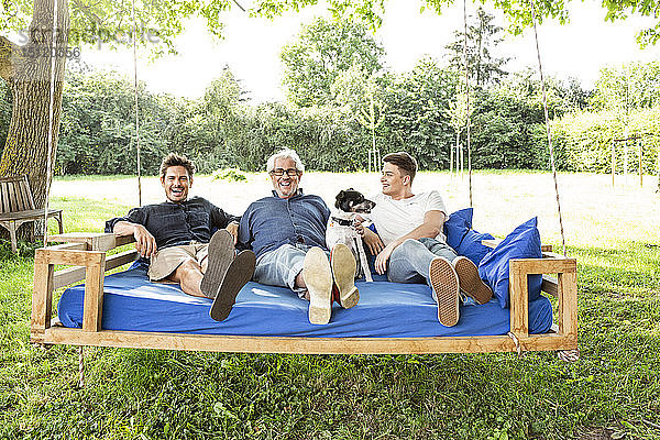 Männer einer Familie sitzen auf einem Schaukelbett im Garten und unterhalten sich