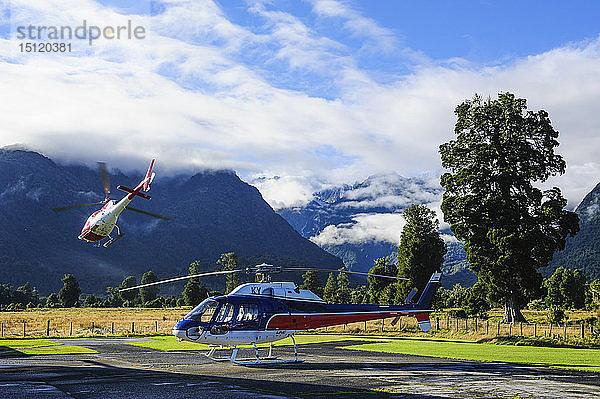 Hubschrauber auf dem Landeplatz  während ein anderer wegfliegt  Fox Glacier  Südinsel  Neuseeland