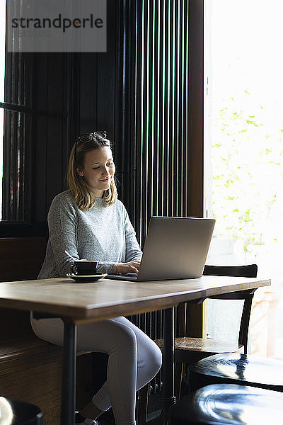 Lächelnde junge Frau mit Laptop in einem Café