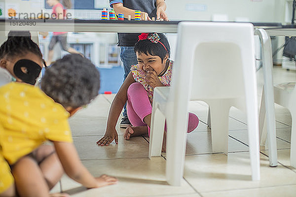 Fröhliche Mädchen spielen im Kindergarten unter dem Tisch