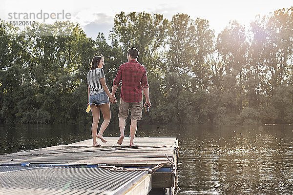 Junges Paar geht Hand in Hand auf einem Steg an einem abgelegenen See