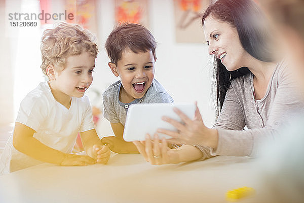 Vorschullehrerin zeigt glücklichen Jungen im Kindergarten eine Mini-Tablette