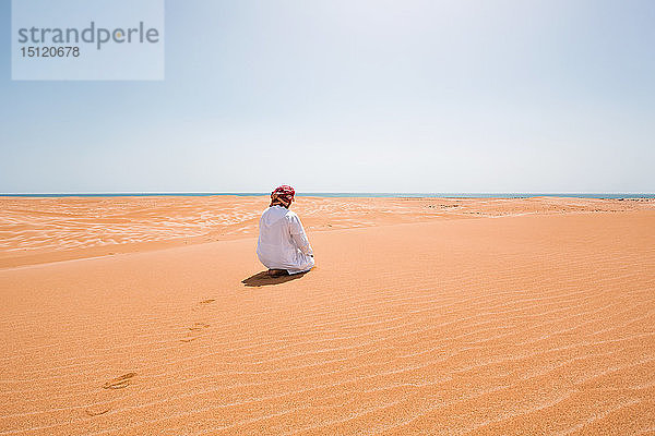 Beduine in Nationaltracht betend in der Wüste  Rückansicht  Wahiba Sands  Oman