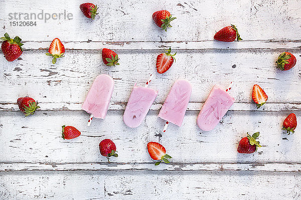 Hausgemachte Erdbeer-Joghurt-Eislollys mit frischen Erdbeeren auf weißem Holz