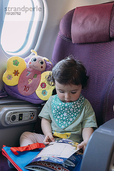Kleinkind Mädchen sitzt im Flugzeug und schaut Bilderbuch