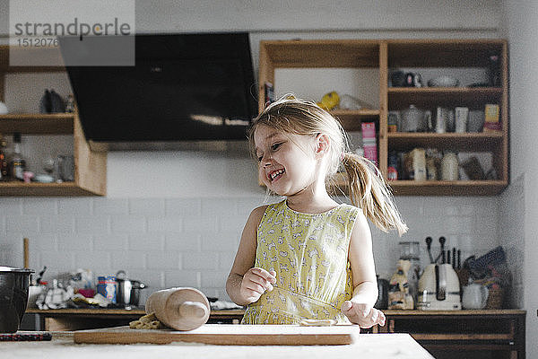 Glückliches kleines Mädchen rollt in der Küche Teig aus