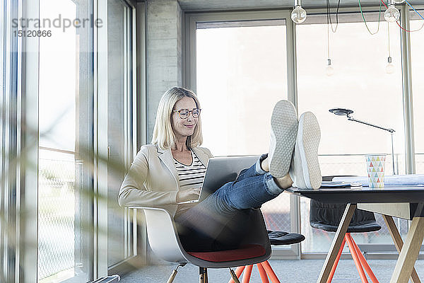 Entspannte Geschäftsfrau mit Laptop im Büro mit hochgelegten Füßen