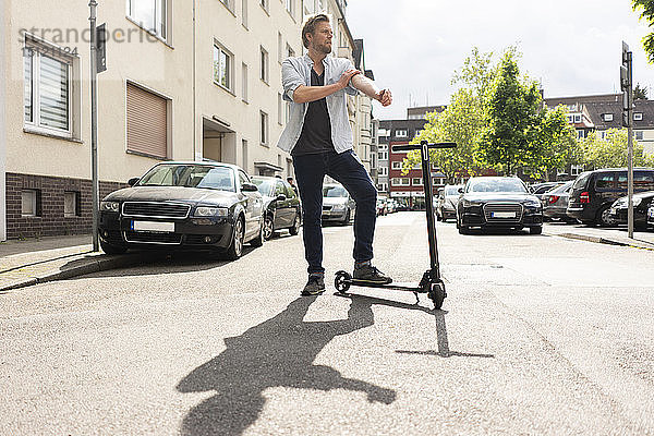 Mann steht mit E-Scooter auf der Straße