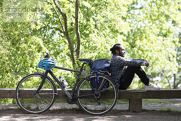 Junger Mann mit Fahrrad entspannt sich auf einer Bank