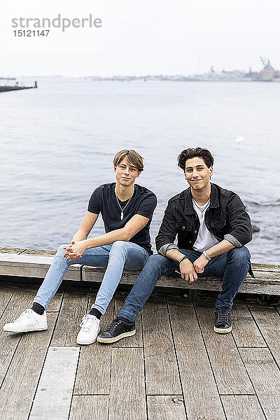 Dänemark  Kopenhagen  Porträt von zwei selbstbewussten jungen Männern  die am Wasser sitzen