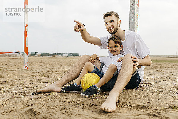 Mann und Junge ruhen sich nach Fußballspiel am Strand aus