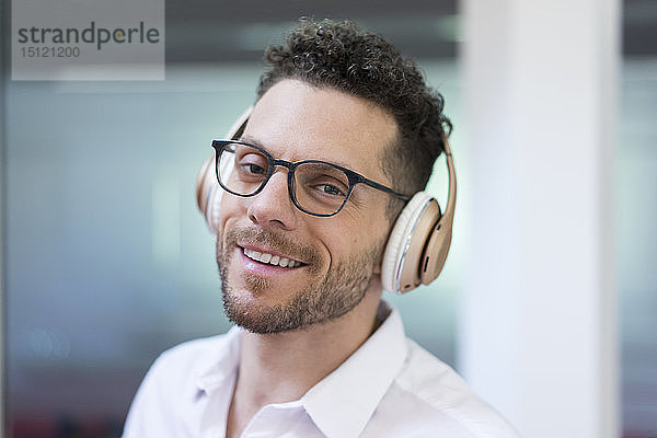 Porträt eines lächelnden Geschäftsmannes  der mit Kopfhörern Musik hört