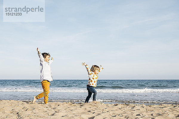 Glücklicher Junge und seine kleine Schwester laufen gemeinsam am Strand