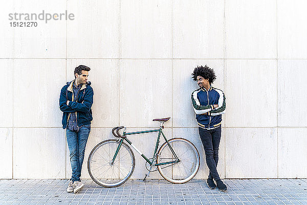 Zwei ungezwungene Männer mit Fahrrad an einer Mauer stehend