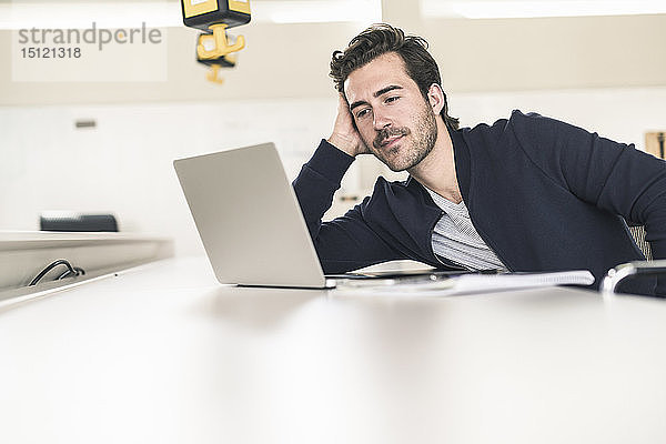 Entspannter junger Geschäftsmann mit Laptop  der im Büro sitzt