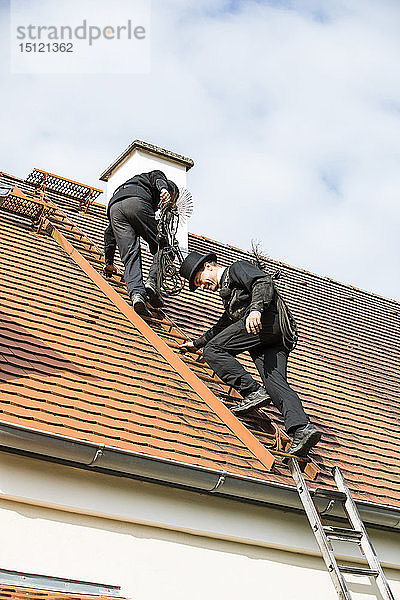 Zwei Schornsteinfeger klettern auf Hausdach